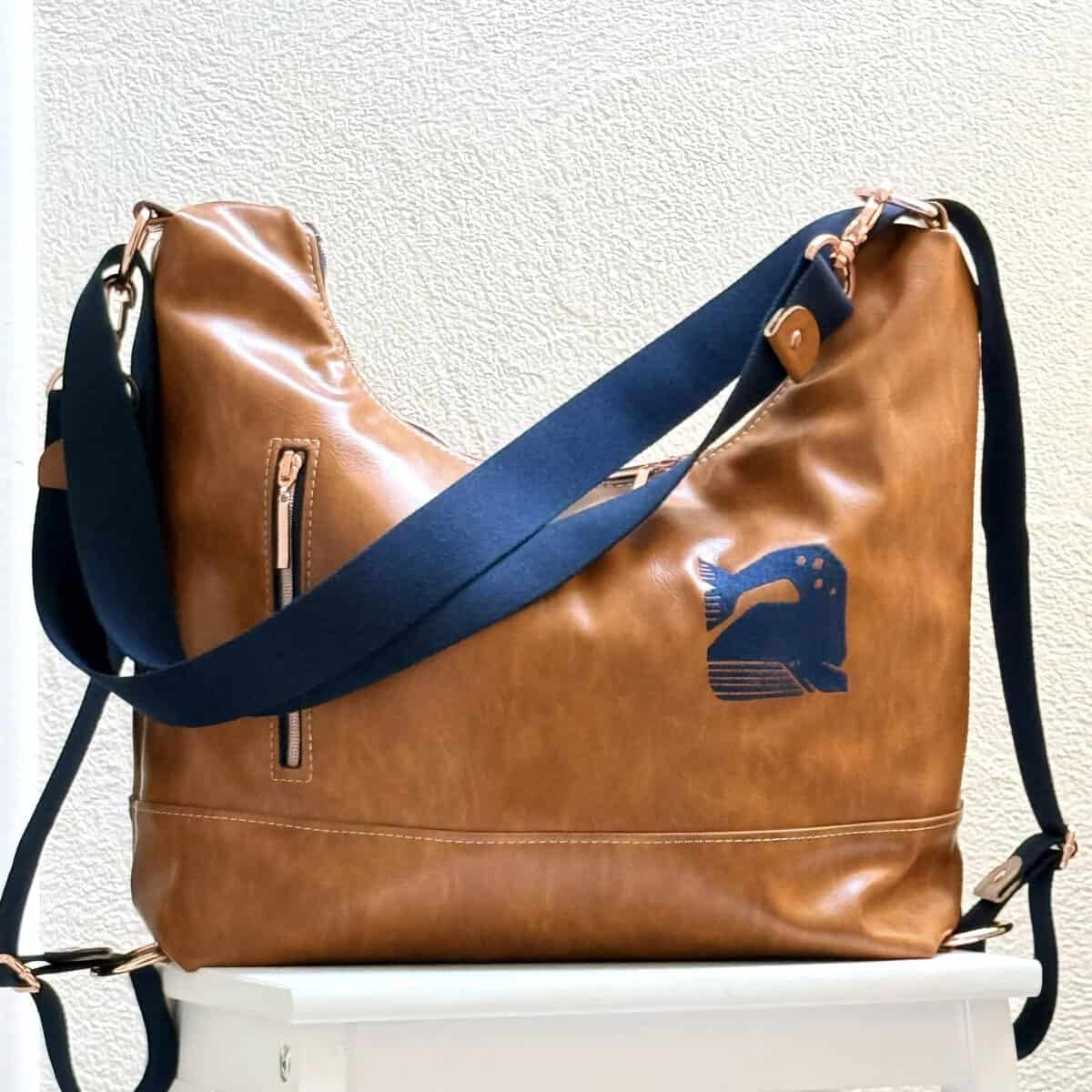 Reisetasche aus braunem Leder mit blauer Schulterriemen und Logo-Print.