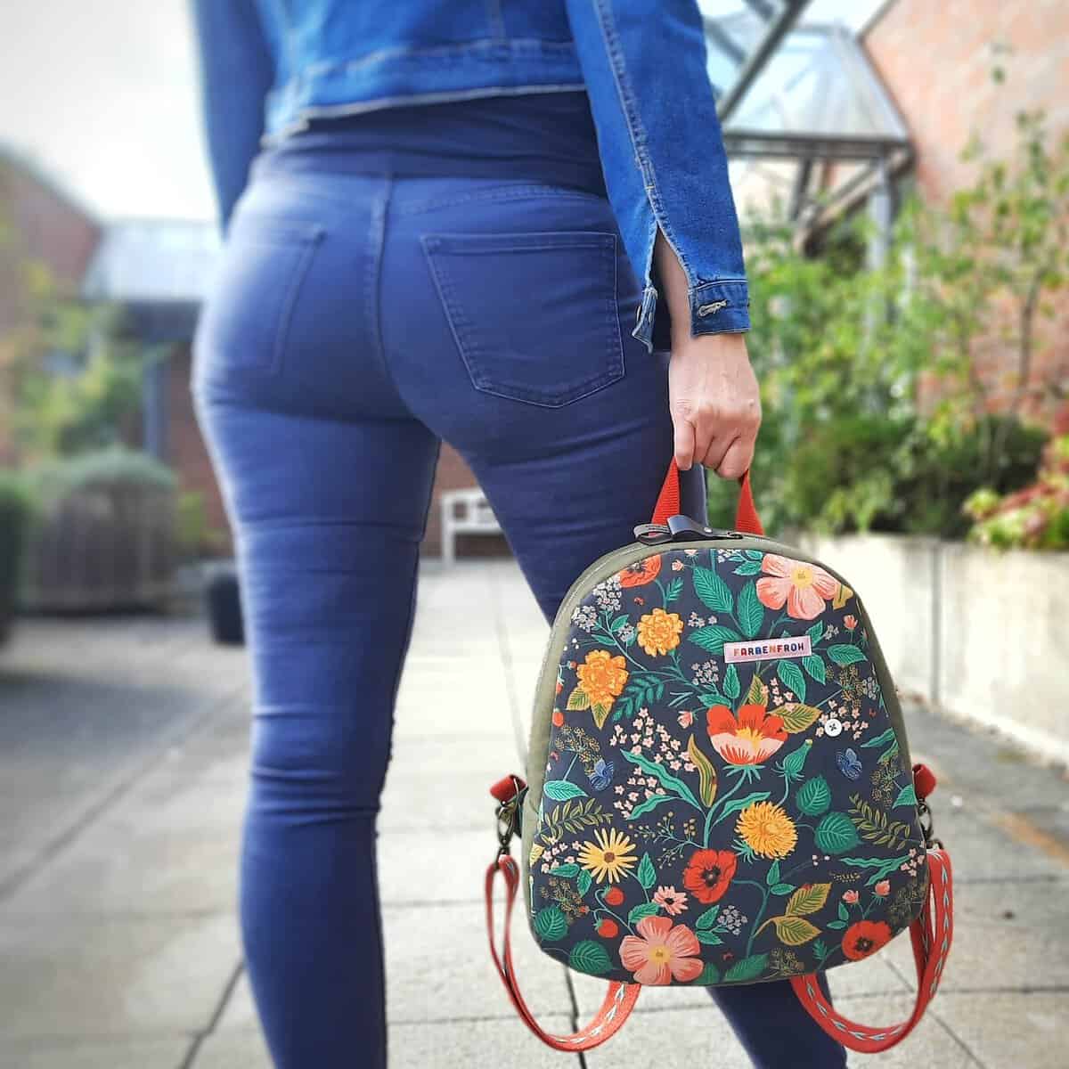 A woman wearing blue jeans and a colorful backpack, standing outdoors.