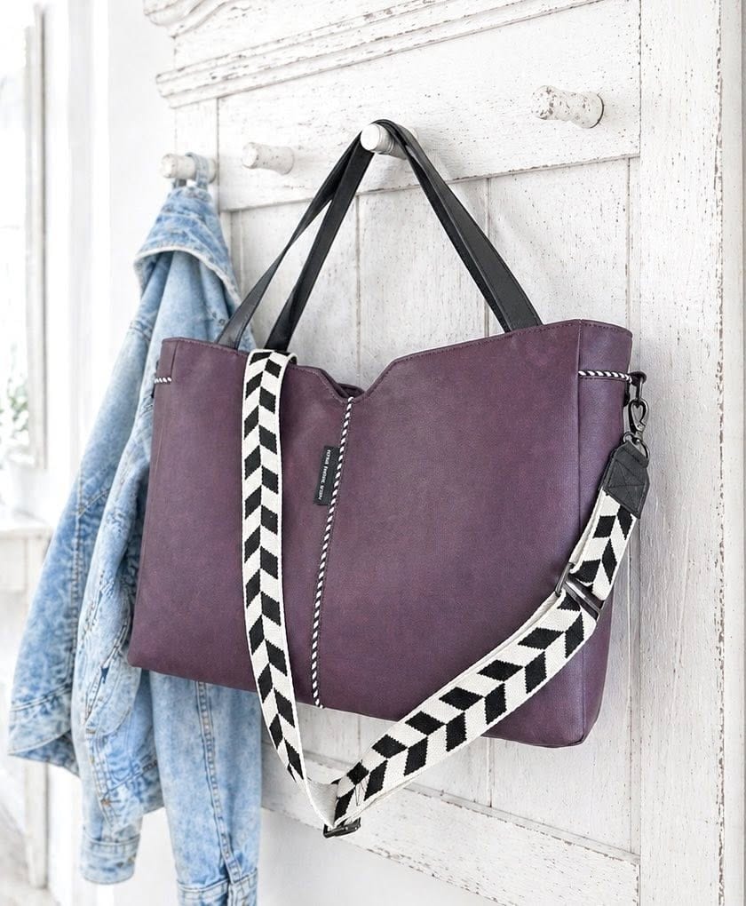 Lila Tasche mit schwarzem und weißem Schultergurt an Wand gehängt.