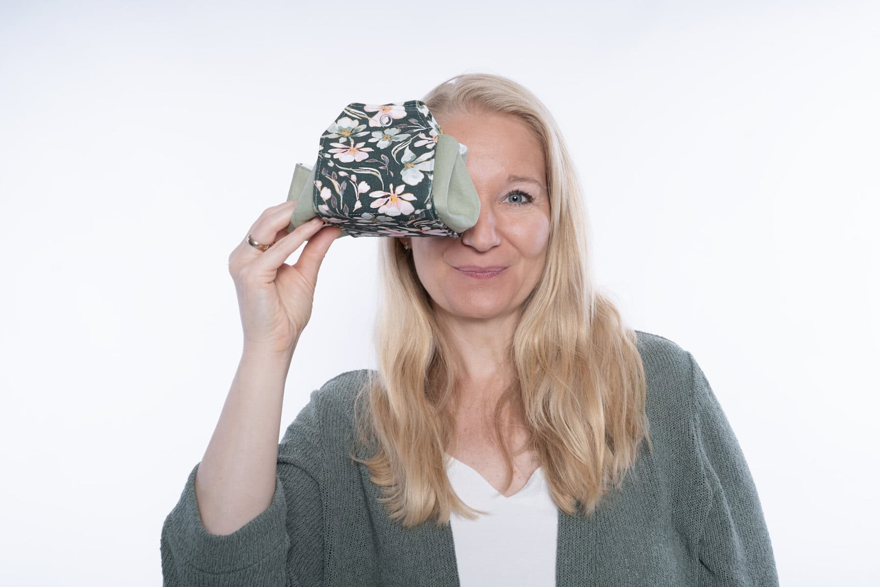 Frau hält Stofftaschentuch vor das rechte Auge, lächelt freundlich.