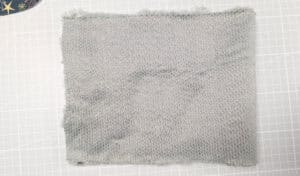 Graues Stoffstück aus recyceltem Material auf weißer Oberfläche.