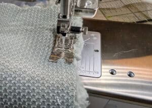 Nähmaschine näht Stoff mit grauem Muster.