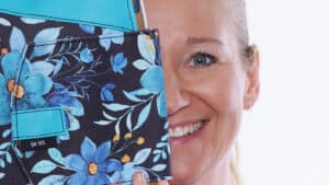 Frau hält eine Tasche mit blumigem Stoffmuster, lächelnd.