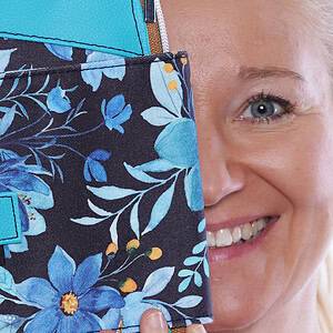 Frau hält eine Tasche mit blumigem Stoffmuster, lächelnd.