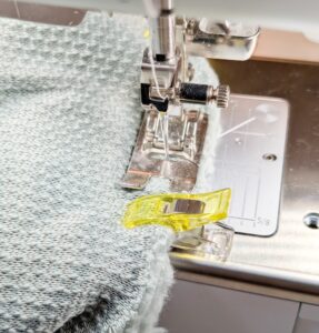 Nähmaschine näht grauen Stoff mit gelbem Clip.