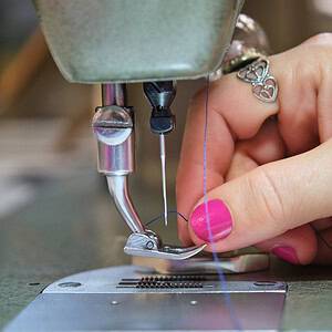 A sewing machine sewing a bag with a blue needle and thread.